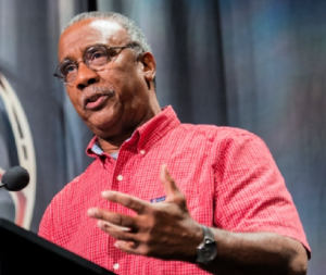 Man in a red shirt speaking at a podium