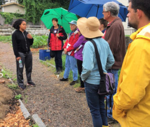 A group of people gathr around a woman speaking at a farm