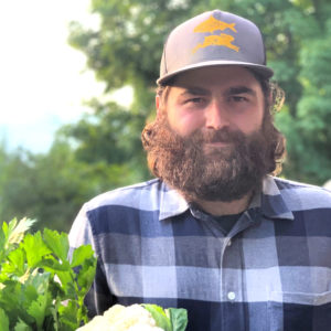 A man in a flannel shirt and blue and gold hat holding vegetables