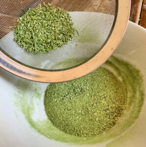 Green powder in a bowl with some being sifted through a mesh strainer