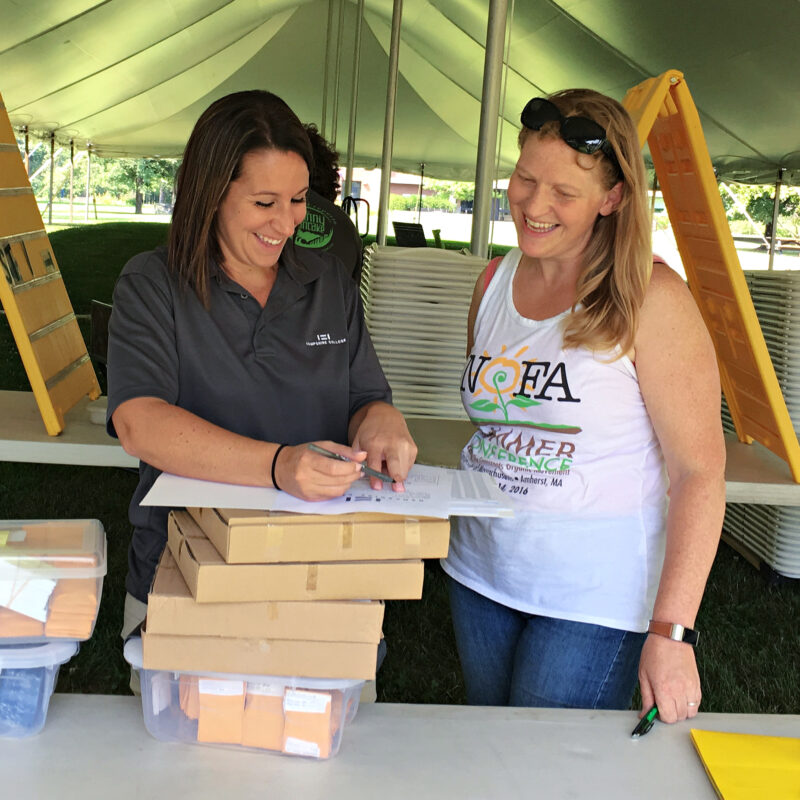 Volunteer – Christine at SC 2016 Two women stand under a tent signing papers