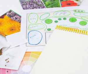 A notebook laying on top of a sketch of a garden plan with seed packets nearby