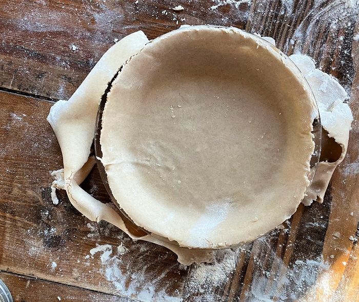A freshly rolled pie crust in a pie plate on a wooden table
